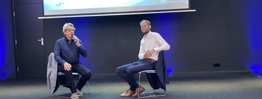 Twee mannen in gesprek op een podium