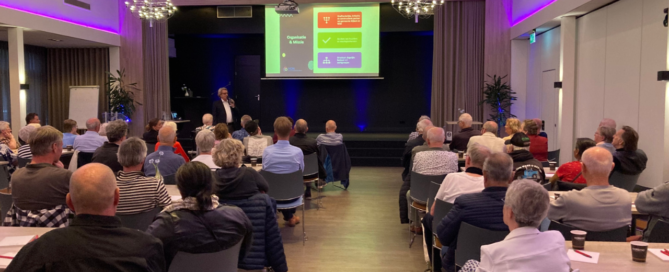 Een volle zaal met huurders luistert naar een spreker die tijdens de jaarvergadering van HON een presentatie geeft over wonen en doorstroming