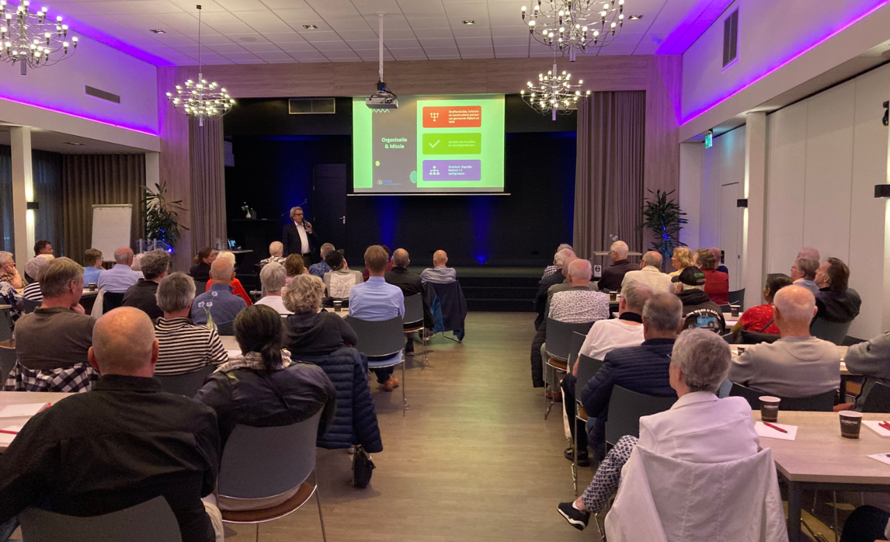 Een volle zaal met huurders luistert naar een spreker die tijdens de jaarvergadering van HON een presentatie geeft over wonen en doorstroming