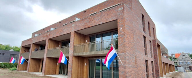Bakstenen appartementencomplex met balkons en Nederlandse vlaggen buiten.