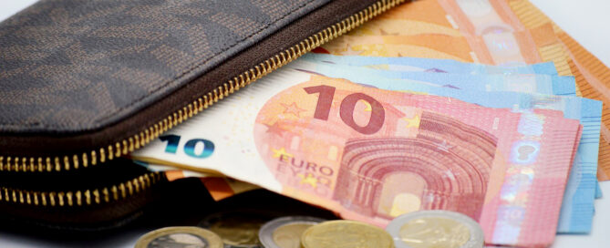 Portemonnee waar eurobiljetten uitsteken, met losse euromunten ervoor op tafel