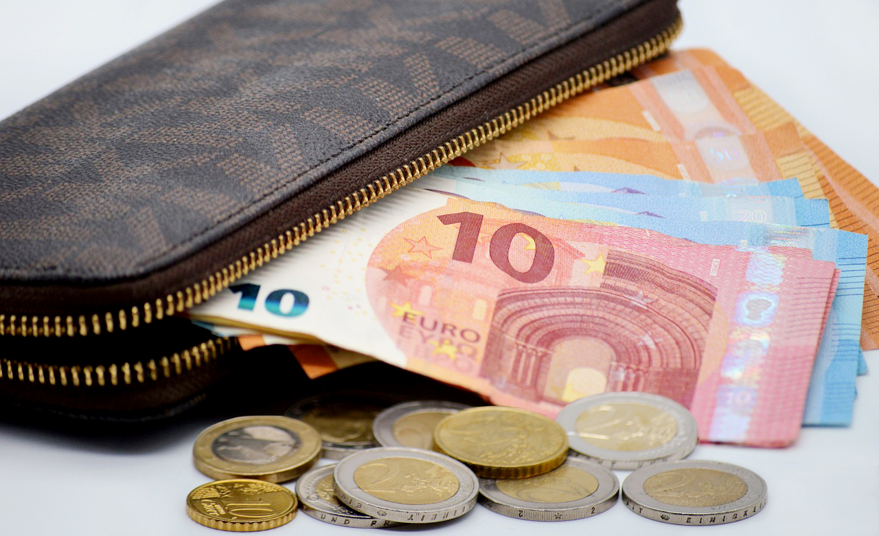 Portemonnee waar eurobiljetten uitsteken, met losse euromunten ervoor op tafel