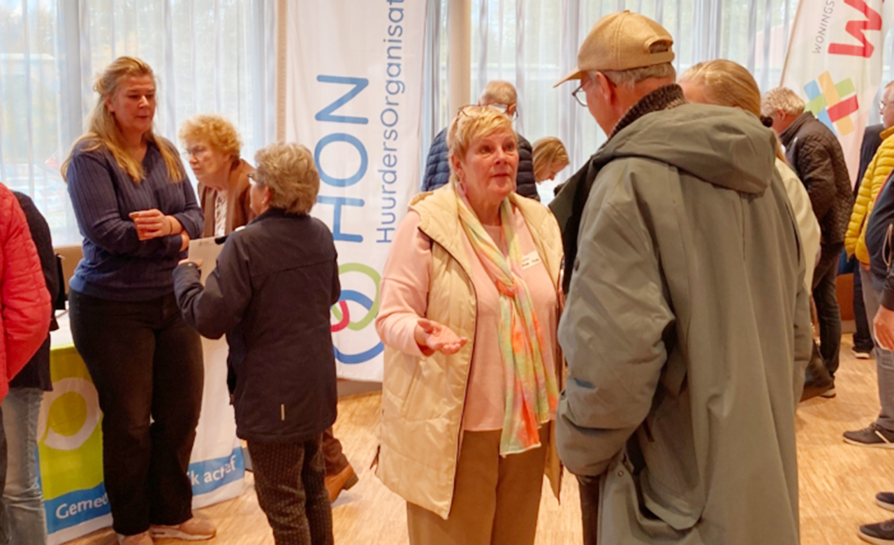 Bezoekers praten met elkaar bij de informatietafel van Huurdersorganisatie Nijkerk en Woningstichting Nijkerk tijdens een drukbezochte bijeenkomst