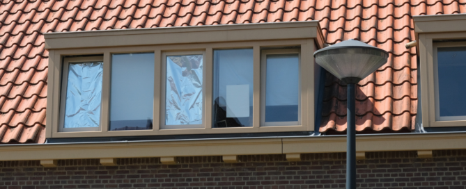 Dakraam van een huurwoning met folie en karton achter de ramen als tijdelijke zonwering tegen de hitte