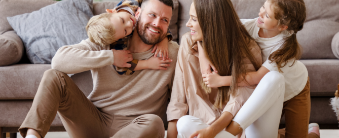 Gezin zit lachend samen op de vloer in een woonkamer en geniet van een moment thuis