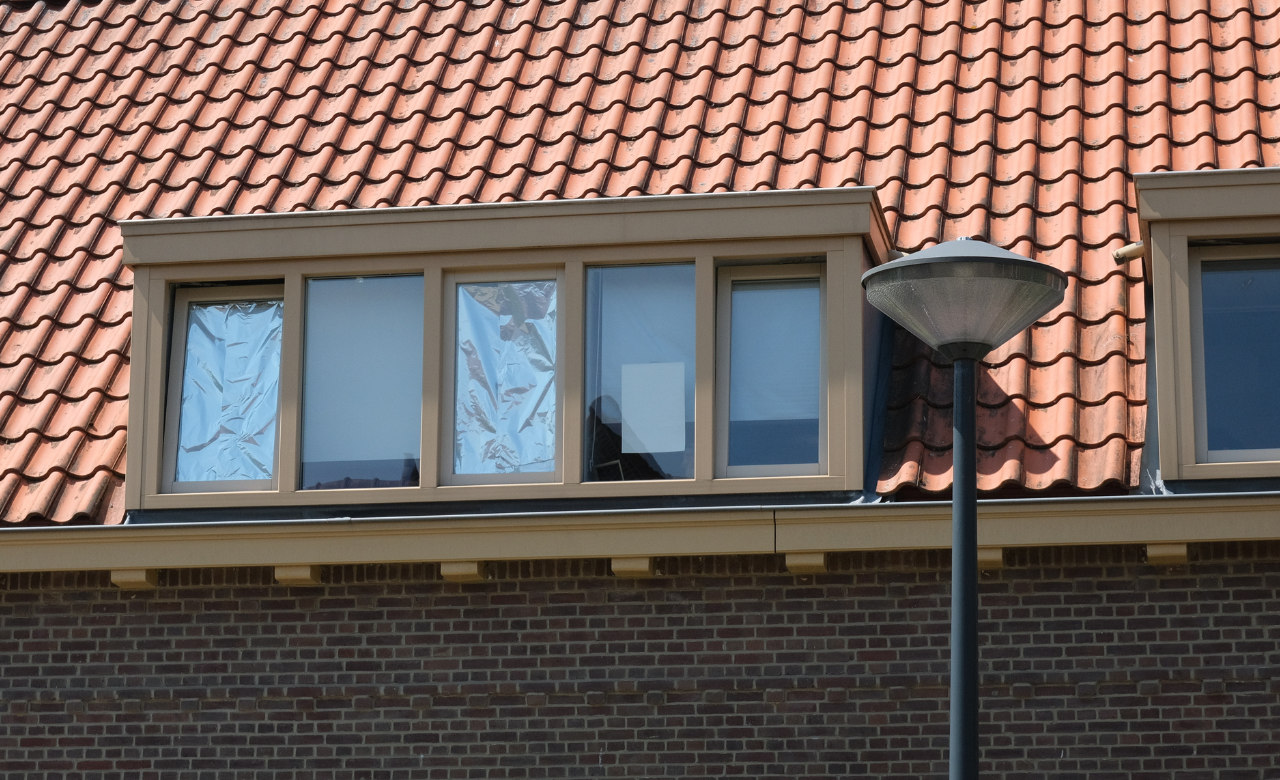 Dakraam van een huurwoning met folie en karton achter de ramen als tijdelijke zonwering tegen de hitte